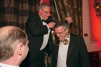 Joe Tierney, helps new president Joe Mannion with his chain